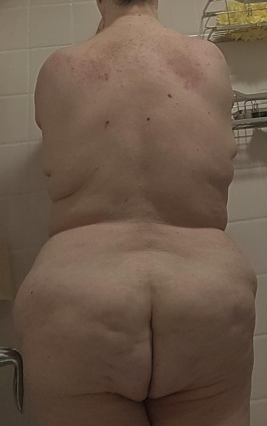 Backside view of my fully naked luscious backside.
My back, butt, thighs fully visible to the audience.
I am standing face forward inside bathroom tub.
I am leaning forward, my hands on bath tile wall.
Photo is cropped from my neck to my lower thighs.